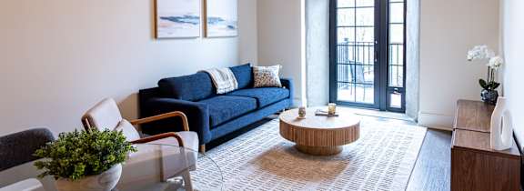 A living room with a blue couch and a glass coffee table. at The Dean at Creekview Apartments, Newark, Delaware
