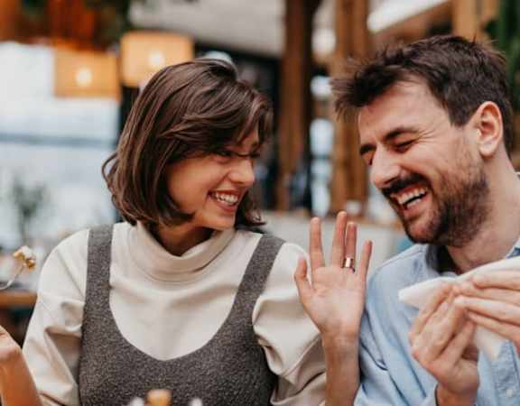 A man and a woman are sitting at a table, sharing a meal and laughing together.
