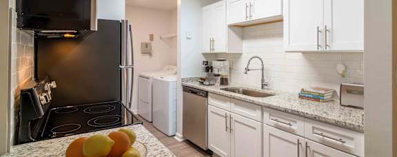 A kitchen with a black fridge, white cabinets, and a bowl of oranges on the counter.