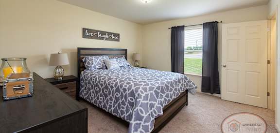 A bedroom with a bed, nightstand, and a rug with the text "Universal Living" on it.