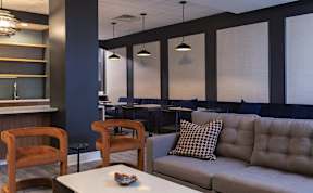 A modern living room with a grey couch, wooden chairs, and a white coffee table.