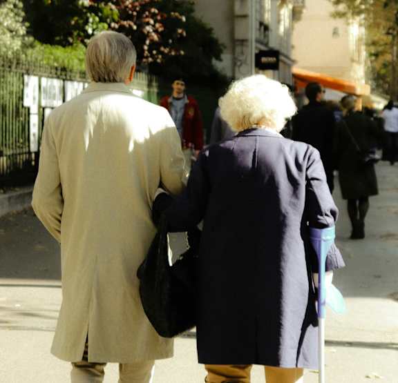 An elderly couple walking down a street holding hands.
