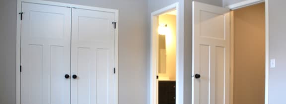 a bedroom with two doors and a bathroom in the background
