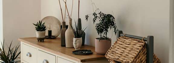 A white potted plant sits on a wooden stool in a room with a white cabinet and a mirror.