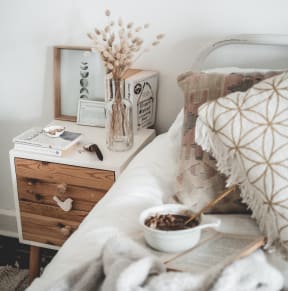 A bedroom with a neatly made bed and a table holding a bowl of coffee.