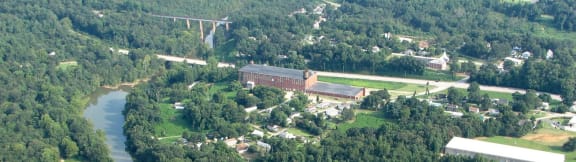Aerial view of Converse Mill Lofts in Spartanburg, surrounded by roads, a river, and trees.