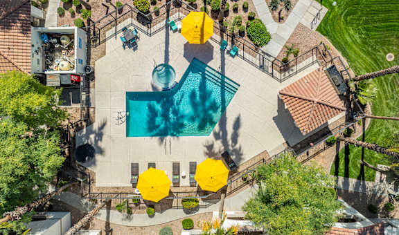 An aerial view of a pool surrounded by yellow umbrellas and palm trees.
