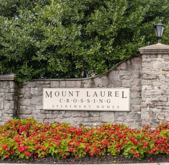 a sign for mount laurel crossing at the entrance of a park with flowers