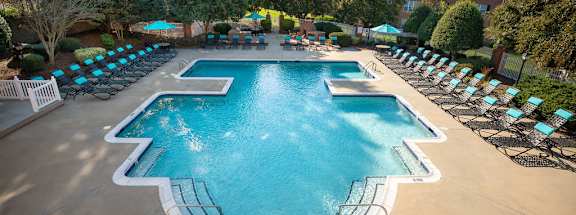 A large outdoor swimming pool surrounded by lounge chairs and trees.