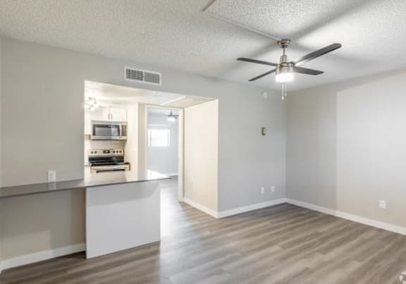 A room with a ceiling fan and a kitchenette.