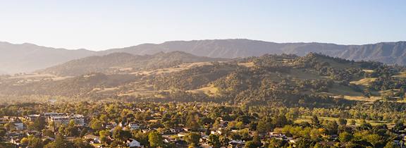 A small town with houses and trees in the foreground and mountains in the background.