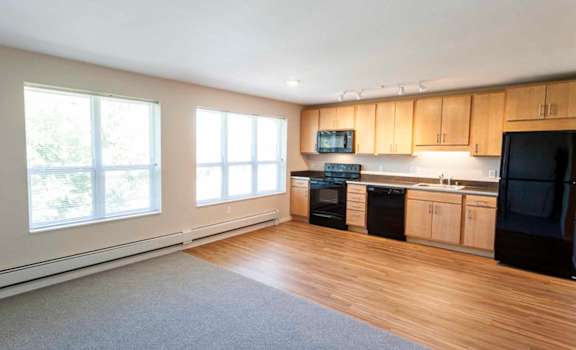 an empty living room with a kitchen in the background