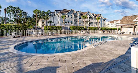 A large outdoor swimming pool surrounded by a stone patio and a row of houses.