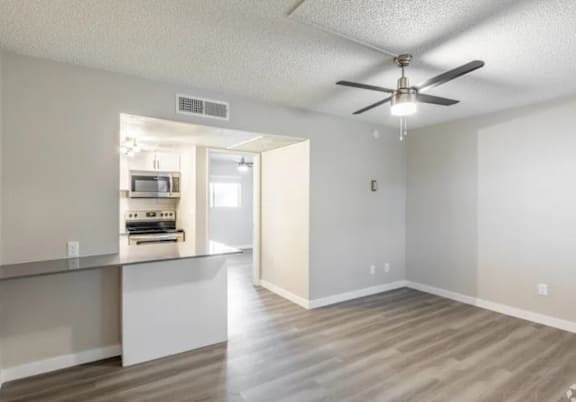 A room with a ceiling fan and a kitchenette.