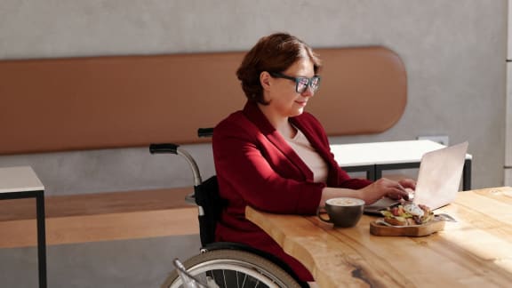 a woman in a wheelchair sitting at a table with a laptop