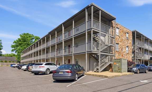 A parking lot with cars and a multi-story building with balconies.