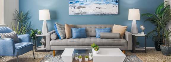 A living room with a grey couch, a coffee table, and a painting on the wall.