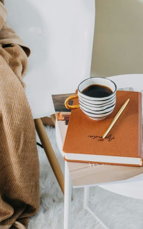 a cup of coffee sitting on top of a book on a chair with a blanket