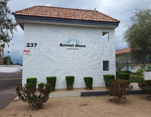 A white building with a red tile roof and a sign that says Sunset Mesa Apartments.