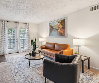 A living room with a brown leather couch, a black armchair, a coffee table, and a painting on the wall.