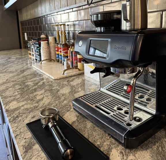 A coffee machine with a portafilter and a tamping tool on a black tray.