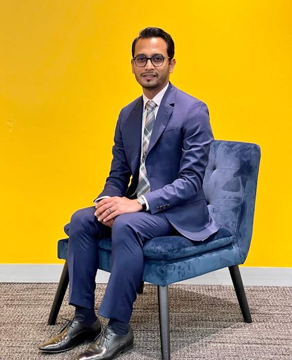 A man in a blue suit sits on a blue chair.