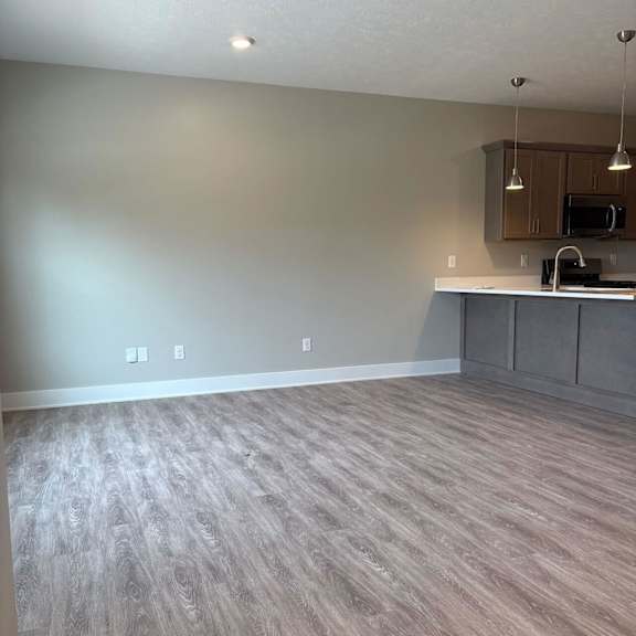 A room with a wooden floor and a kitchenette in the background. at Ventura Townhouses, Michigan, 49460