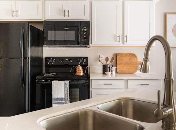 A modern kitchen with a black refrigerator and stove, white cabinets, and a stainless steel sink.