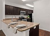 Thumbnail 6 of 28 - A kitchen with brown cabinets and a granite countertop.