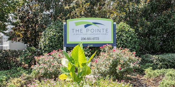 a sign for the pointe in a garden with bushes and trees