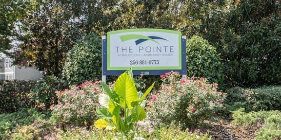 a sign for the pointe in a garden with bushes and trees