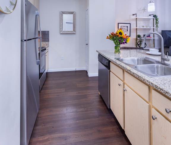 A kitchen with a refrigerator, sink, and wooden floors.
