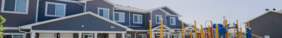 A playground with a blue slide and yellow poles is in front of a building with multiple windows and doors.
