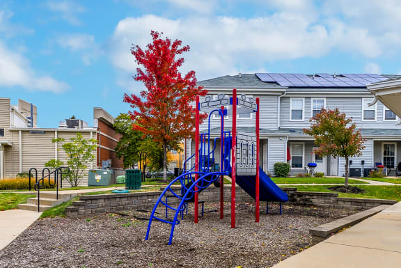 a playground with a blue and red swing set in front of houses