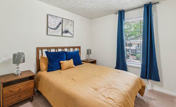 A bedroom with a bed, nightstand, and window with blue curtains.