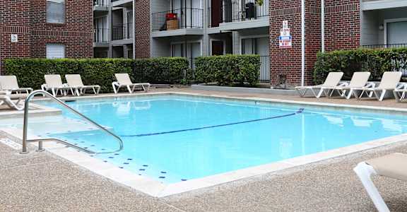 A pool surrounded by lounge chairs in front of apartment buildings.