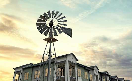 A windmill stands in front of a building with a blue sky in the background.
