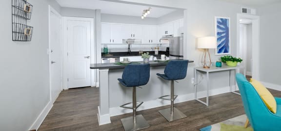 View of kitchen in Mandarin bay apartment in Jacksonville from living room. Kitchen has a two-seater island dinette with modern bar height stools.