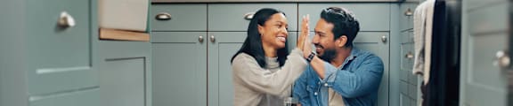 A man and woman sitting on the floor in a kitchen, giving each other a high five.