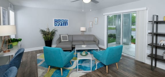 Living room in Mandarin Bay apartments in Jacksonville, FL with midcentury modern grey and blue seating, ceiling fan, and blue, green, and grey rug.
