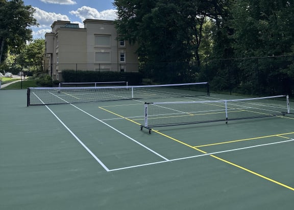 a tennis court with trees and a building in the background at Stuart Woods* Apartments, Virginia, 20170