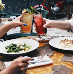 Two people toasting with drinks at a table with food.