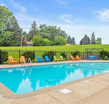 A large outdoor swimming pool surrounded by a fence and lounge chairs.