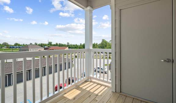 A balcony with a white door and a red car parked in the parking lot.