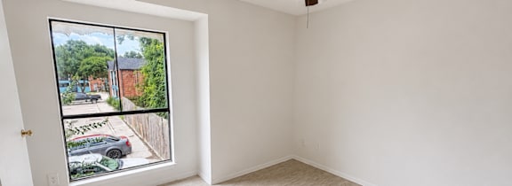 A room with a ceiling fan and a window overlooking a parking lot.