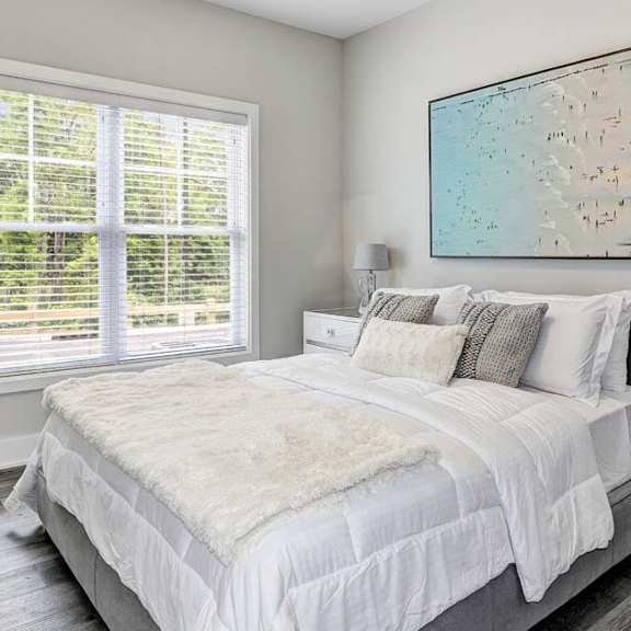 A bedroom with a large bed, a white chair, and a painting on the wall.