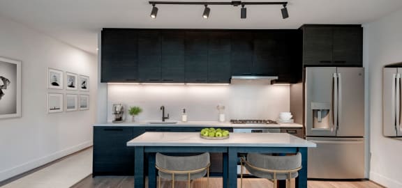 a kitchen with black cabinets and a blue island with three chairs
