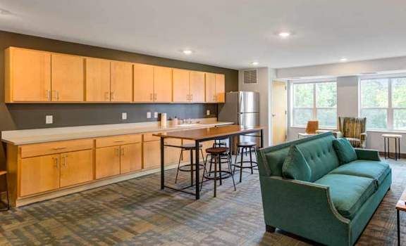 a living room with a couch a table and chairs and a kitchen with a refrigerator