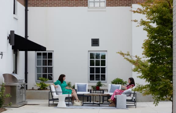 two women sitting on chairs on a patio outside a building