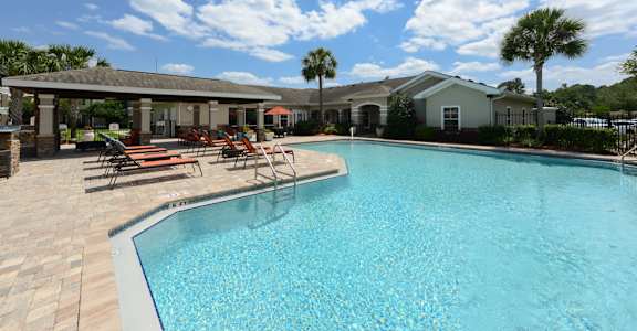 A swimming pool surrounded by a patio with chairs and a building in the background.